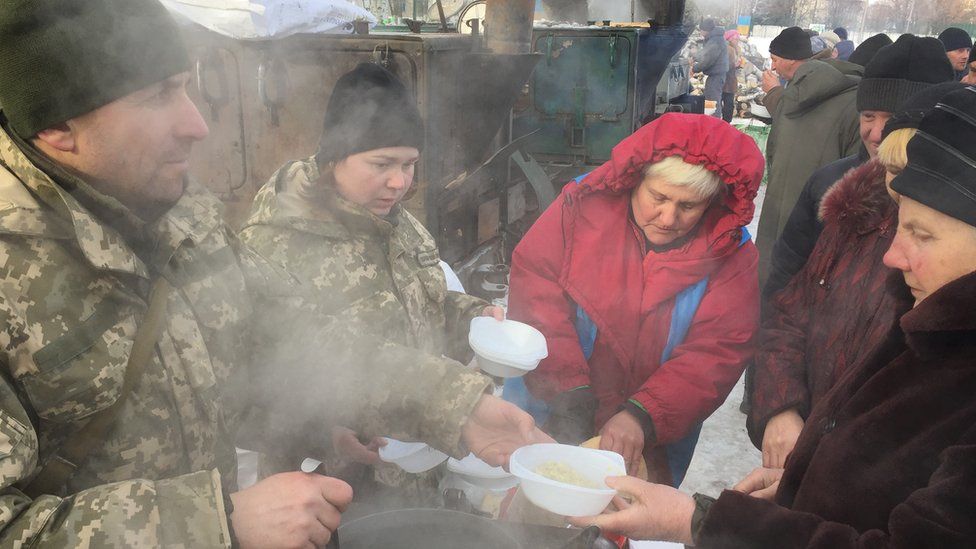 Ukrainian soldiers hand out hot stew to queues of people at temporary aid camp in Avdiivka
