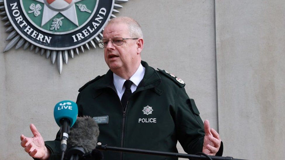 Police Service of Northern Ireland Chief Constable Simon Byrne speaks into a microphone in front of a PSNI crest