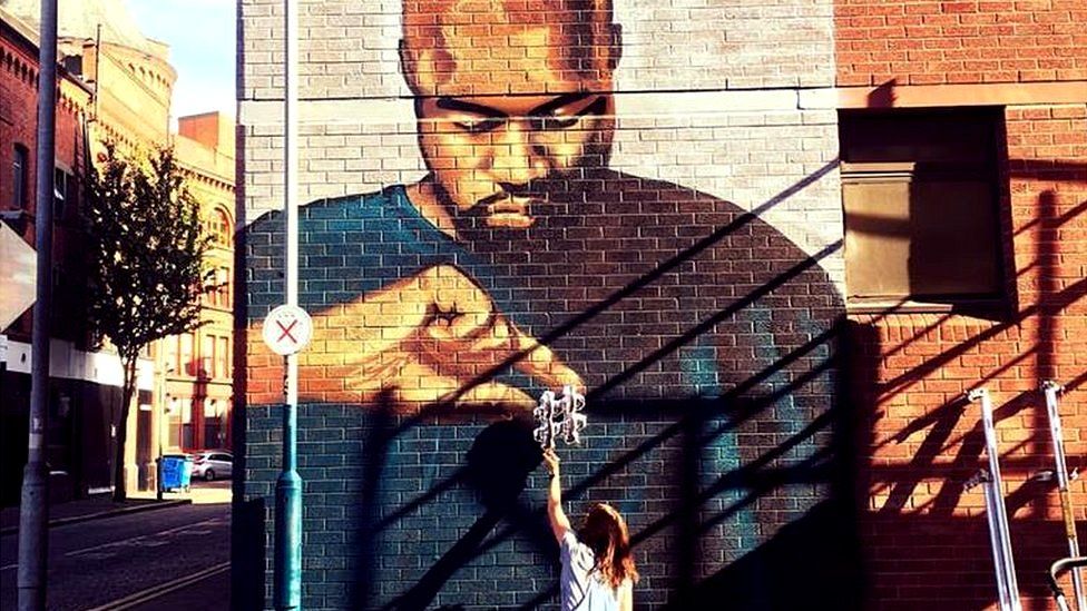 a girl reaching up to a hashtage held by a portrait of kanye west