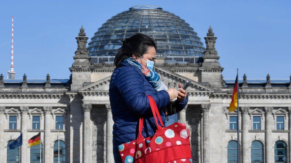 Woman walks past Reichstag wearing a mask