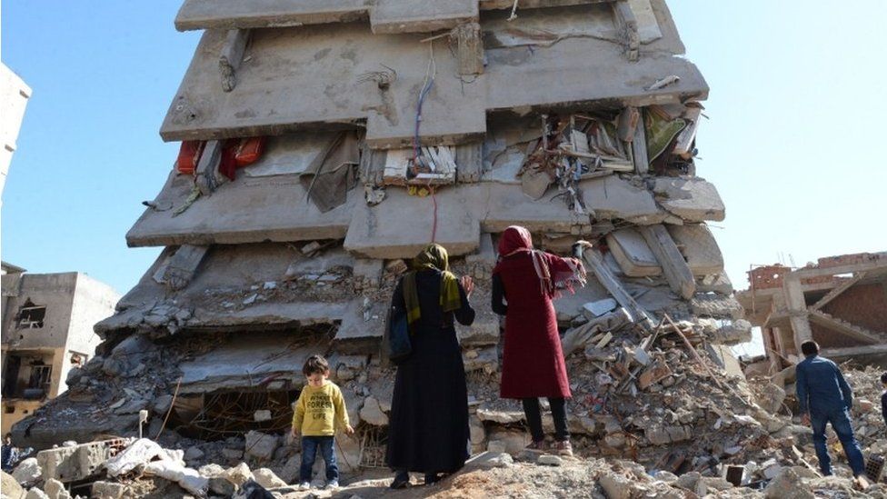 People stand among the rubble of damaged buildings following heavy fighting between government troops and Kurdish fighters in the Kurdish town of Cizre on 2 March 2016
