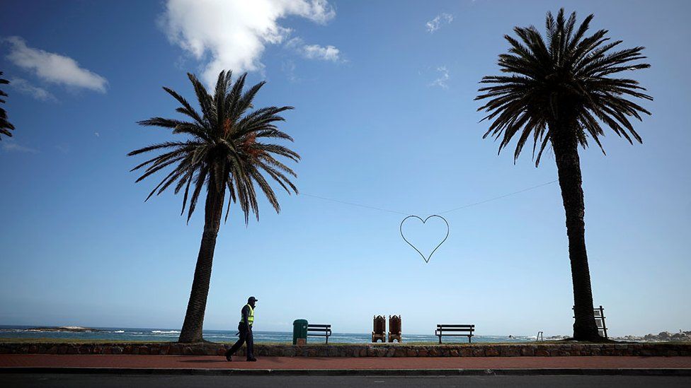 A security guard walks under palms at a deserted Camps Bay beach, South Africa