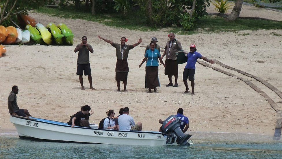Hotel staff greet tourists arriving on a Fijian island by boat
