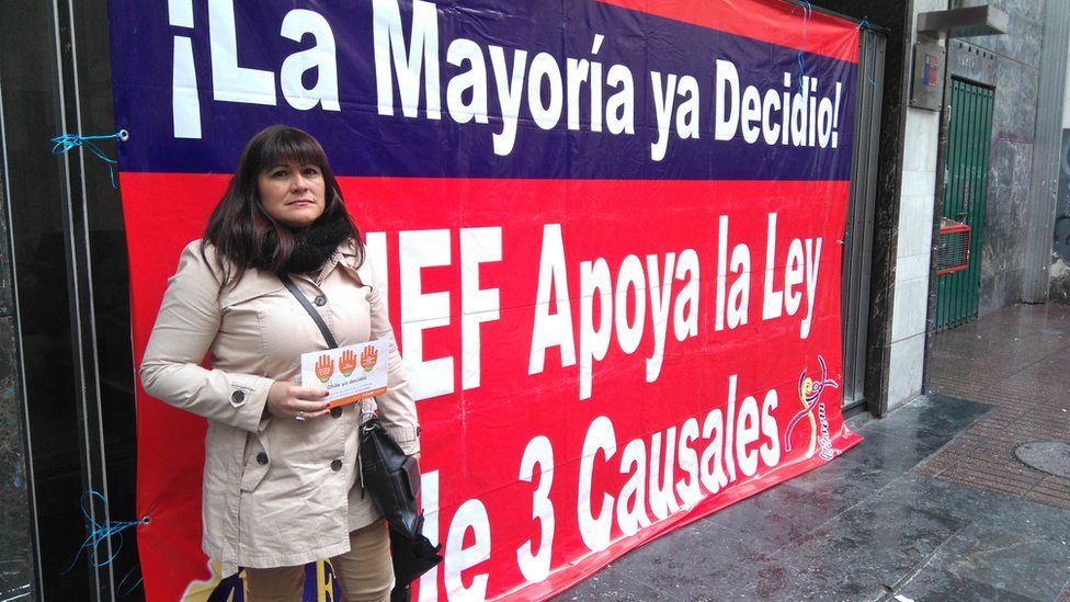 Paola Valenzuela stands in front of a poster backing a change in the law