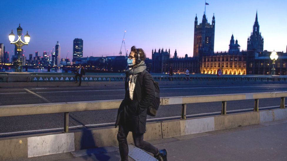 A man wearing a mask crosses Westminster Bridge past the Houses of Parliament