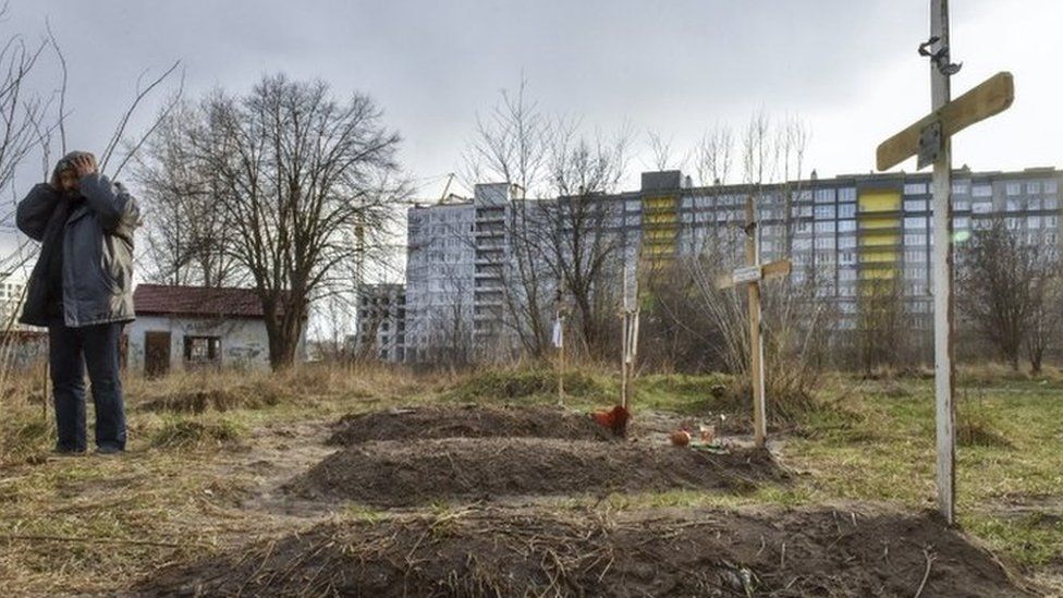 Graves are seen in front of a residential building in Bucha