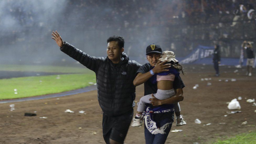 Two men evacuate a girl at Kanjuruhan stadium in Malang, Indonesia. Photo: 1 October 2022