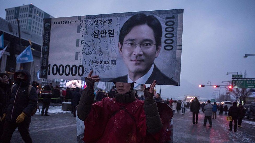 Протестующий держит плакат с изображением лица наследника Самсуна Ли Джэ Ёна на антиправительственном протесте против коррупции в 2017 г.