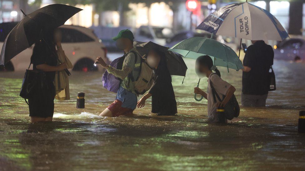 People wade though an inundated road in southern Seoul, South Korea, 08 August 2022 (issued 09 August 2022), as heavy rainfall of over 100 millimeters per hour, the heaviest in 80 years, battered Seoul and surrounding areas.