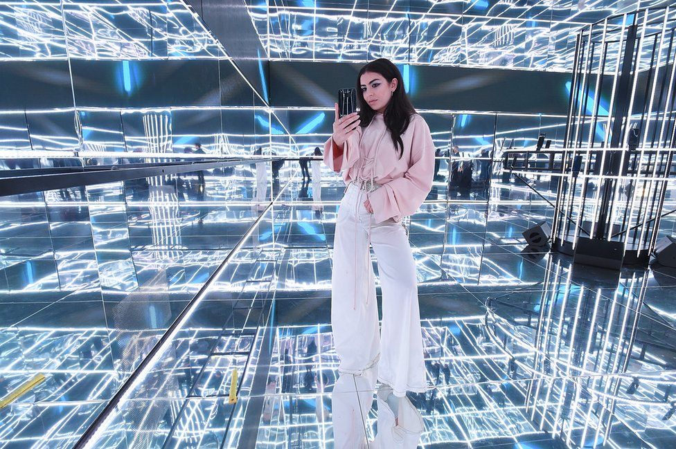 Charli XCX takes a photograph in a mirrored cube