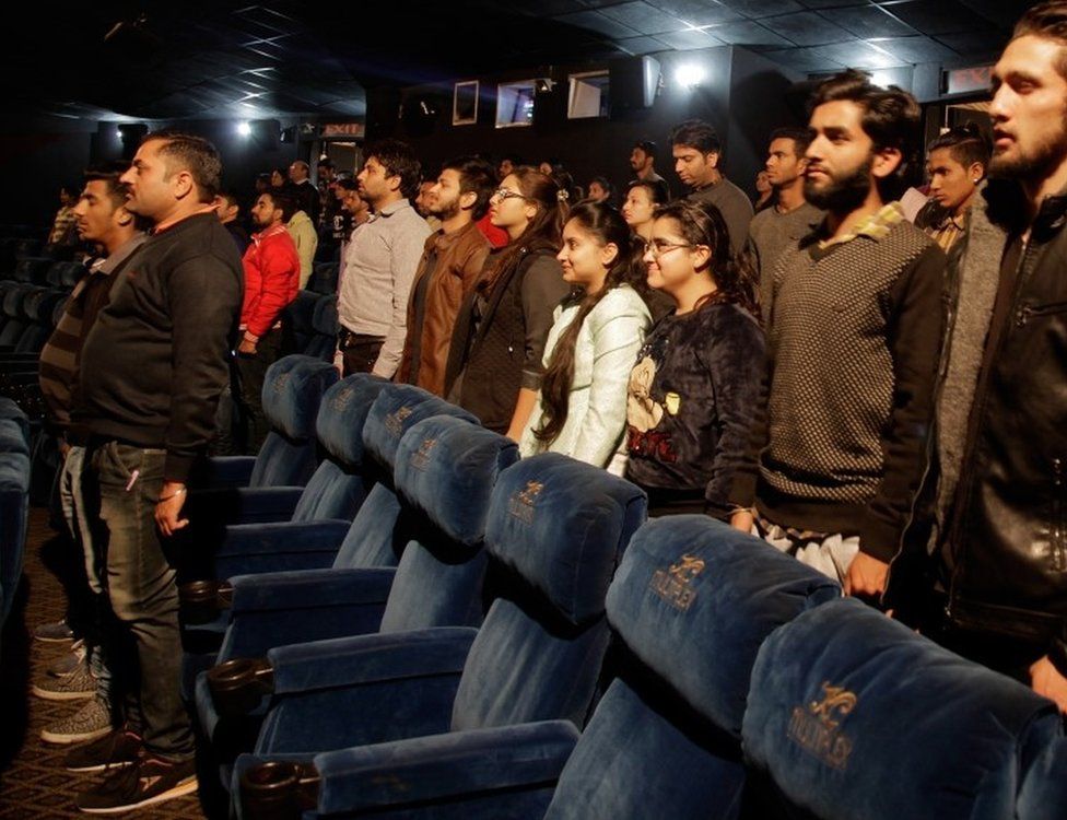 Indian movie goers stand up as national anthem is played at a movie hall before the screening of a movie in Jammu, India, Tuesday, Dec. 13, 2016.