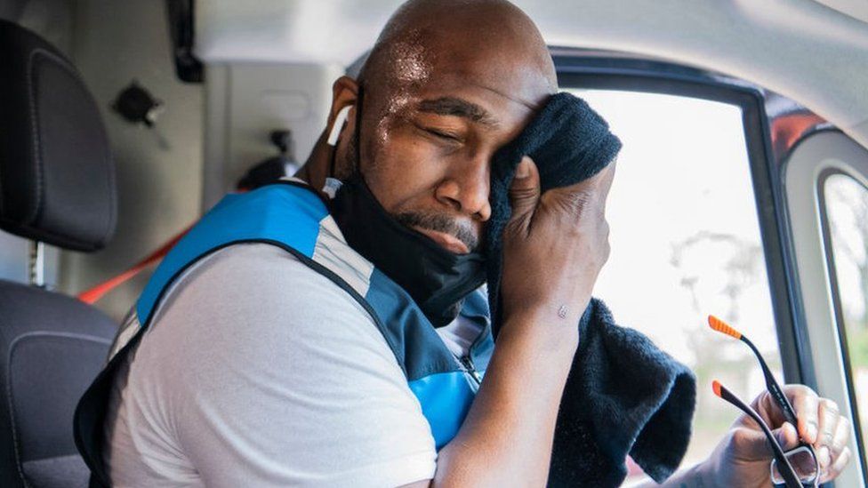 Man in a lorry cab wiping sweat from his brow with a towel