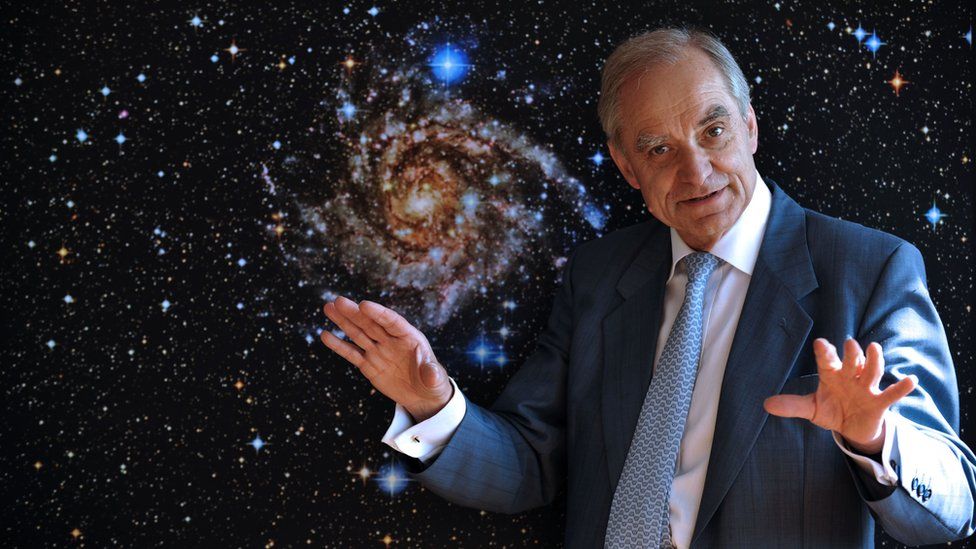 This file photo taken on May 19, 2009 shows French astrophysician Andre Brahic posing in front of a picture of the IC 342 galaxy