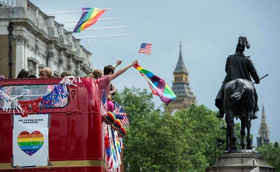 Red bus with people waving rainbow and American flags