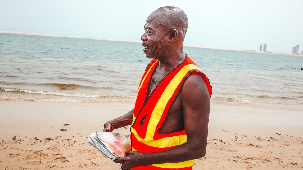 Lifeguard Samuel Omohon holds photos on a beach in Lagos, Nigeria