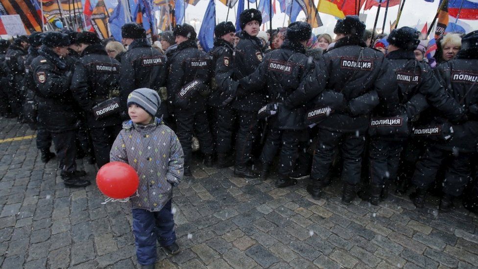 Boy stands in front of Russian police officers during festive concert marking second anniversary of Russia"s annexation of Crimea in central Moscow