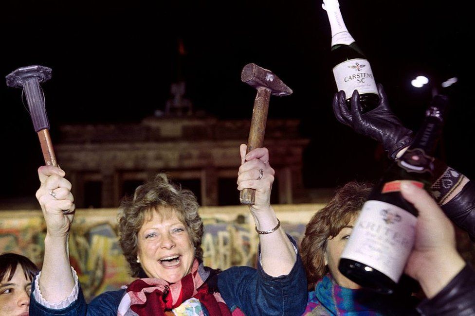 A berliner holds up a hammer and a chisel early on November 15, 1989 in front of the wall at the Brandebourg Gate partly visible behind it as a crowd of people demonstrated for the destruction of the wall for a passage way between the East and the West near the monument.