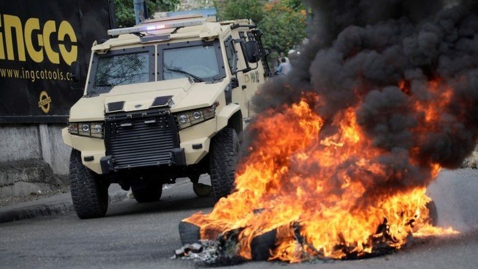 Forças de segurança passam ao lado de um incêndio provocado por manifestantes durante um protesto em Porto Príncipe