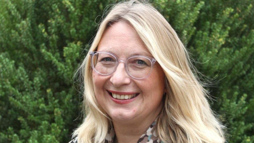 Judi Newman, wearing glasses with blonde hair, smiling at the camera