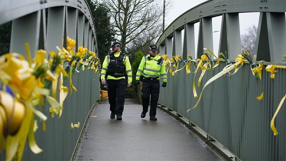 Police officers walk past yellow ribbons tied to a bridge for Nicola Bulley