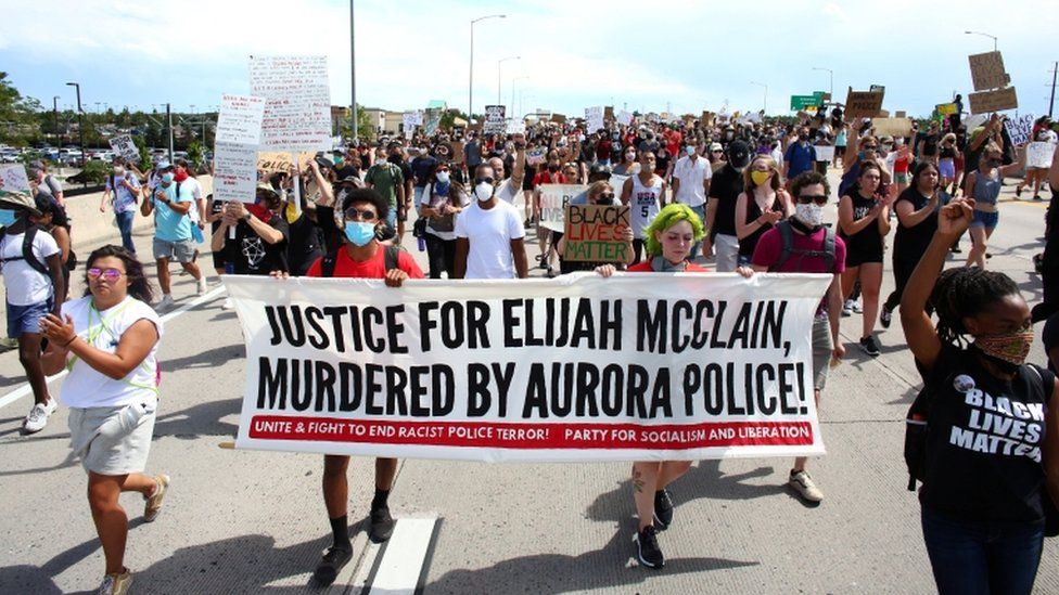 Protesters march holding a banner that reads: "Justice for Elijah McClain, murdered by Aurora Police!"