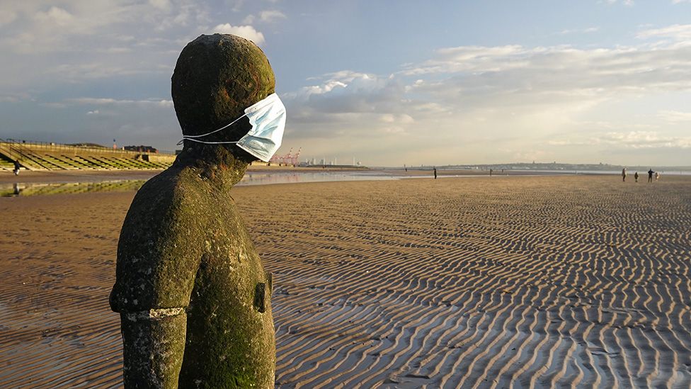 An Anthony Gormley statue on Formby Beach, Merseyside, wearing a mask