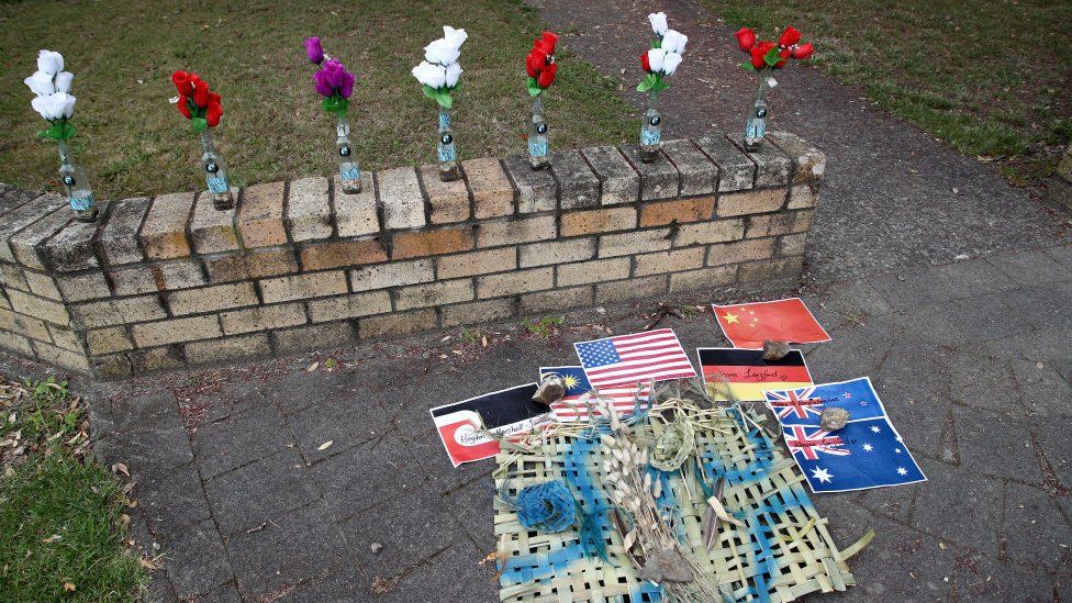 A small tribute memorial in the New Zealand town of Whakatane shows flowers and the flags of countries where victims were from