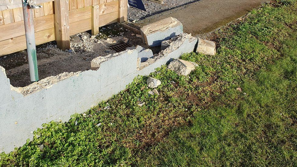 A concrete wall partially destroyed next to some grass