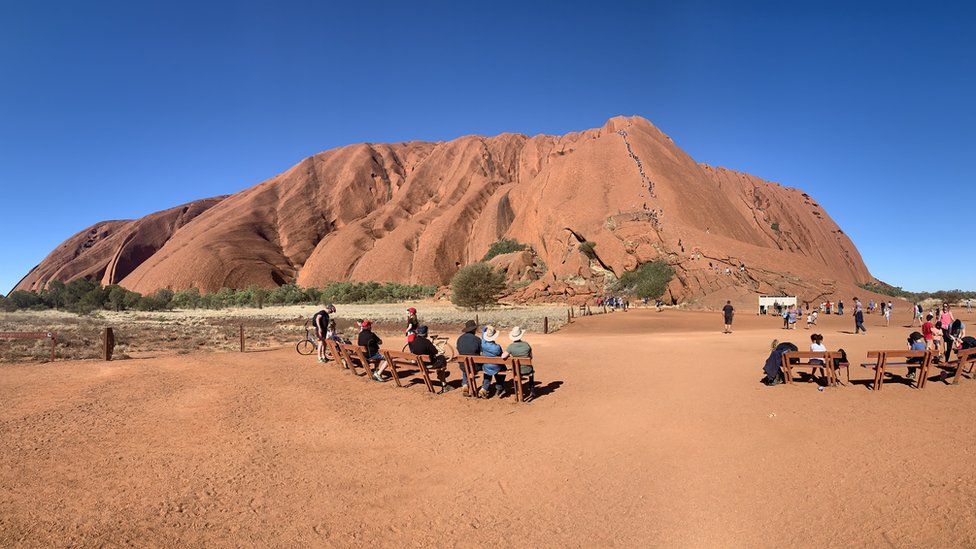 Locals watch on as tourists climb Uluru