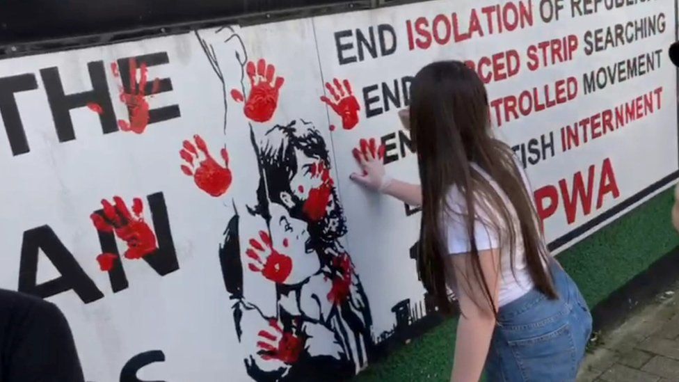 A woman smears a red hand print on a wall