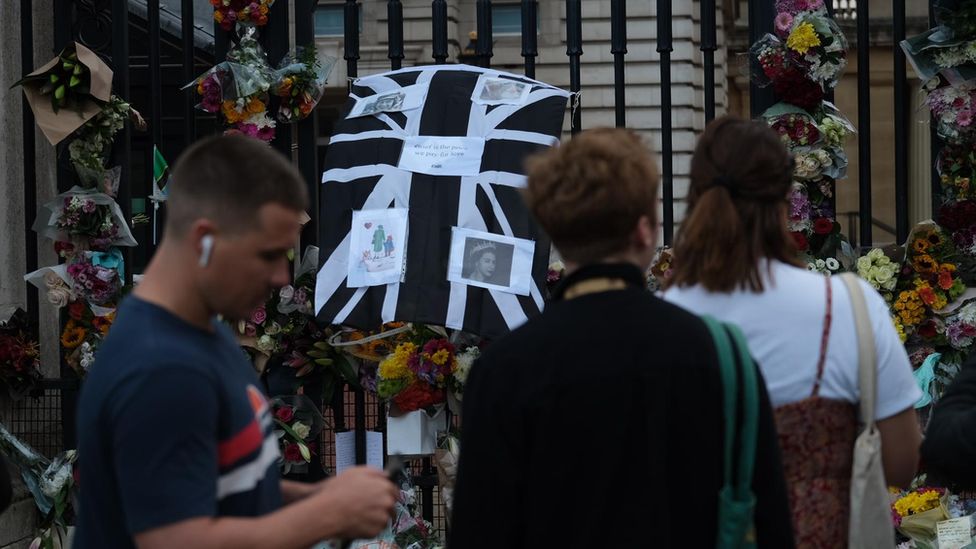 People standing in front of tributes to the Queen in front of Buckingham Palace