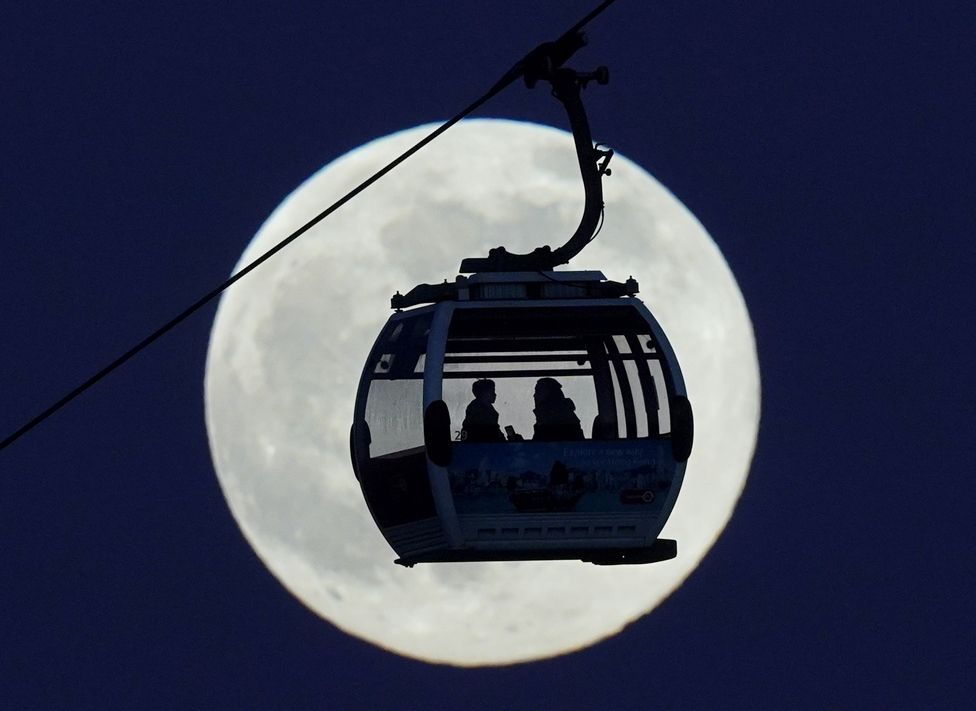 A cable car passes in front of the moon as it crosses the River Thames, London, on 17 January 2022