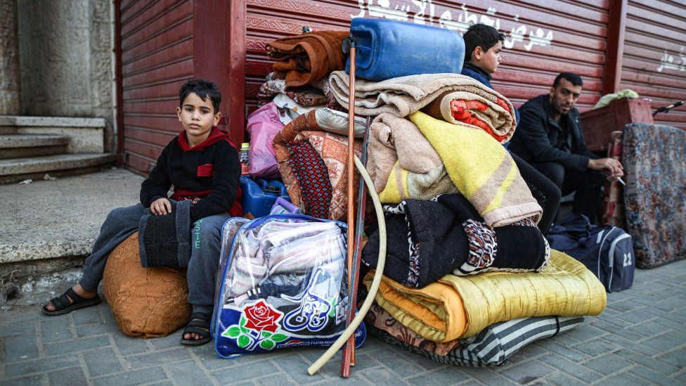 Two children and a man are pictured with a pile of belongings in the street