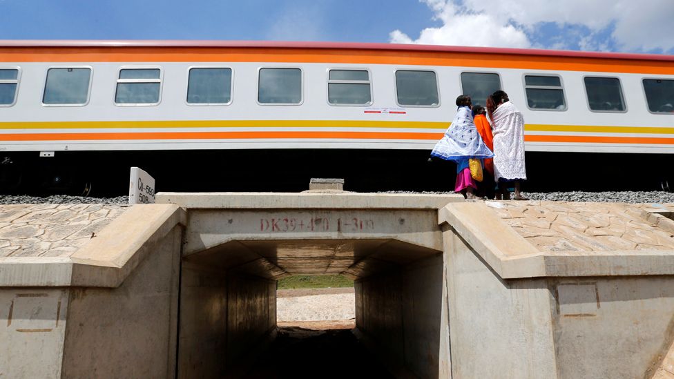 Women stand next to a train on the Standard Gauge Railway line in Kimuka, Kenya - 2019