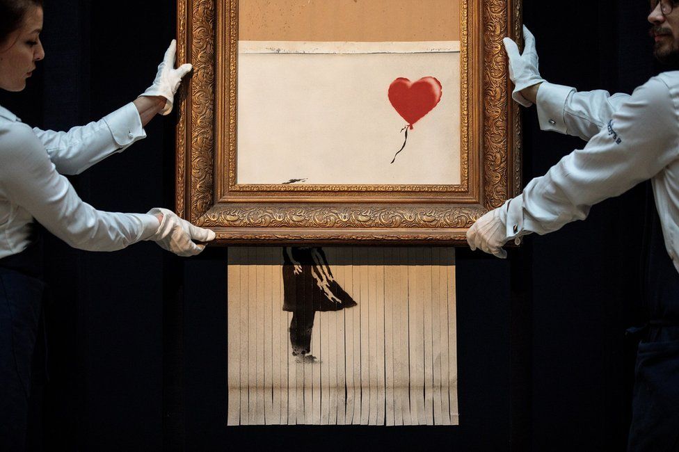 Sotheby's employees pose with Love is in the Bin by British artist Banksy
