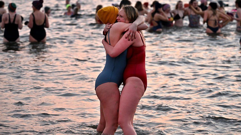 Женщины обнимаются в море в купальных костюмах.