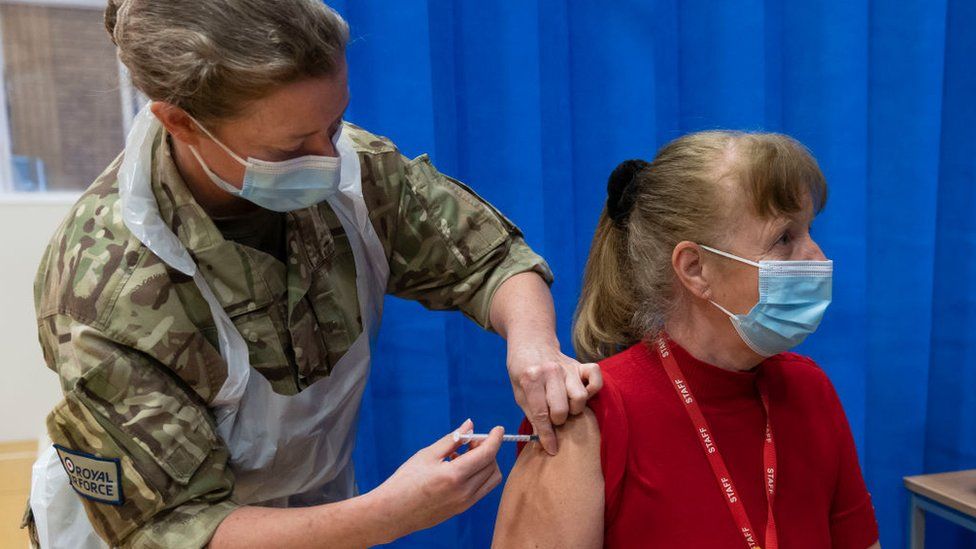 A member of military vaccinating a woman with the AZ jab