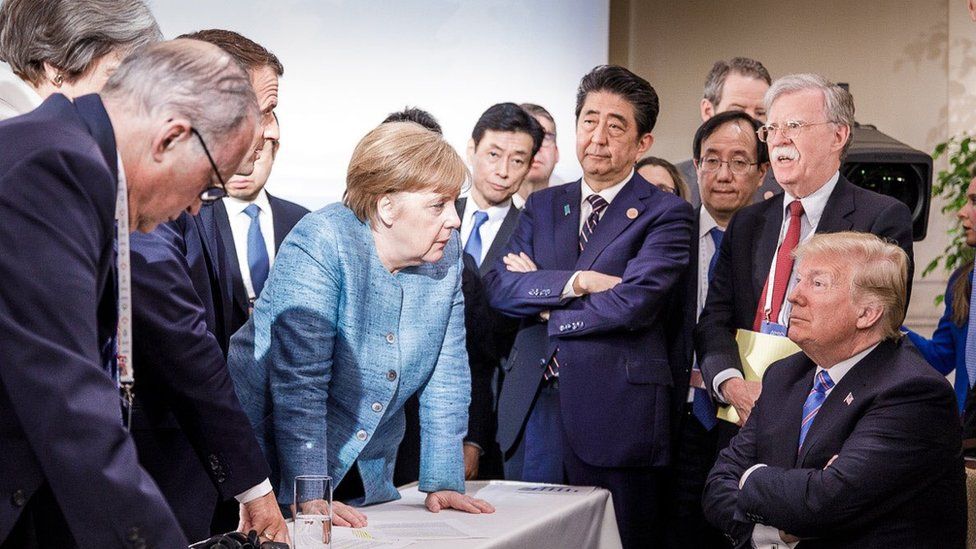 US President Donald Trump talking with German Chancellor Angela Merkel and surrounded by other G7 leaders during a meeting of the G7 summit