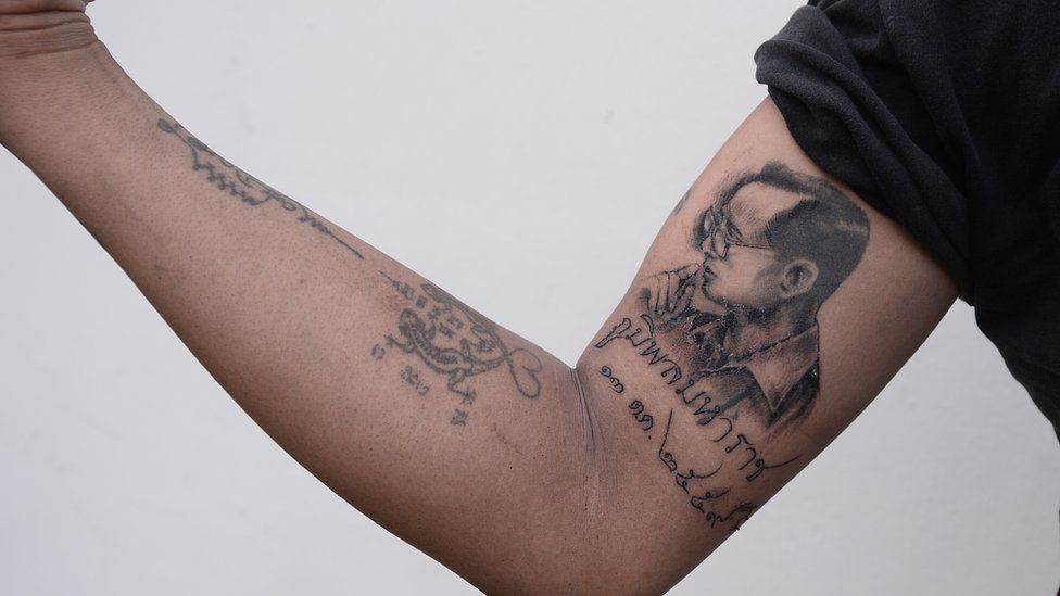 A man flexes his arm showing a portrait tattoo of King Bhumibol