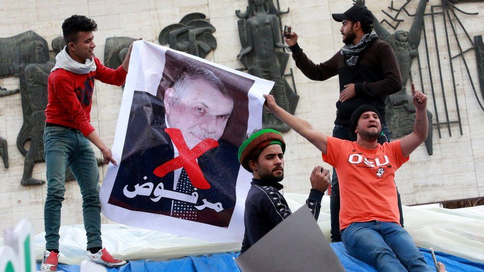 Iraqi hold up a poster showing former Prime Minister-designate Mohammed Allawi and the word "rejected" in Tahrir Square, Baghdad (1 March 2020)