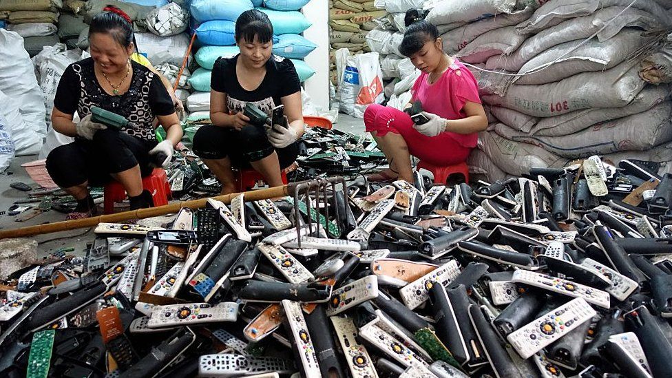 A group of women sorting through old TV remotes in Guiyu, China