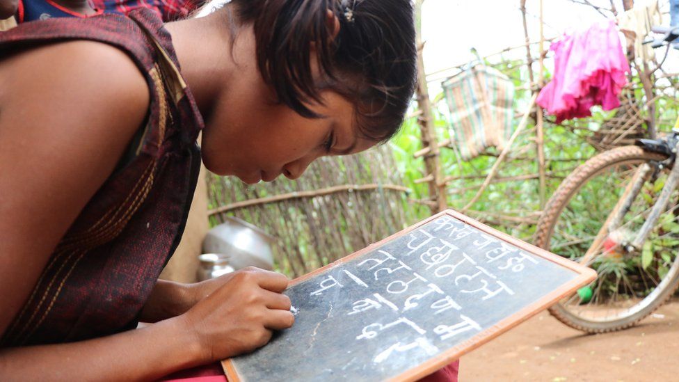 Radhika writing the Hindi alphabet on a slate.