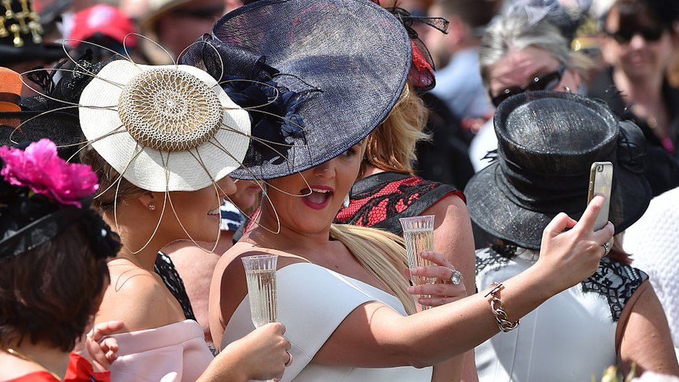 Dressed-up racegoers wearing elaborate hats pose for a selfie at the Melbourne Cup in 2018