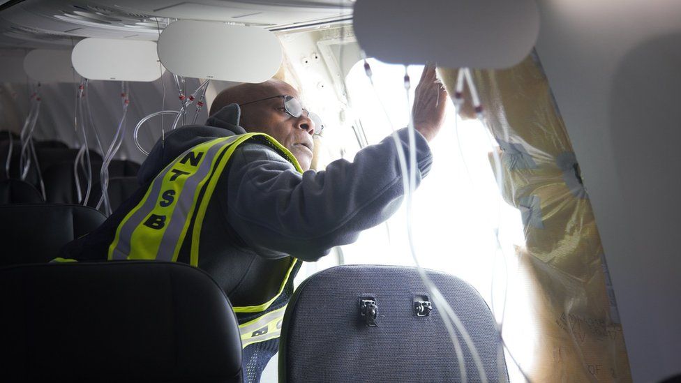 An NTSB employee inspects damage on board an Alaska Airlines plane