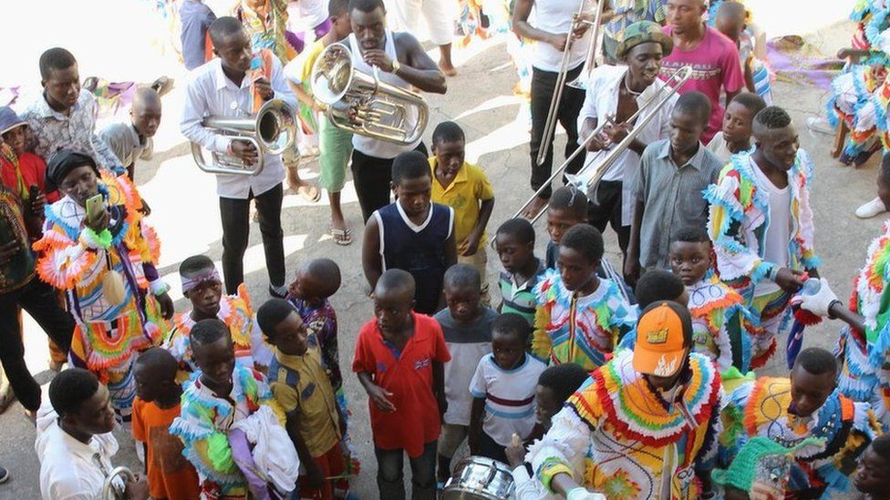 Men carry trumpets, surrounded by a group of young children, before the start of the parade in Sekondi Ghana