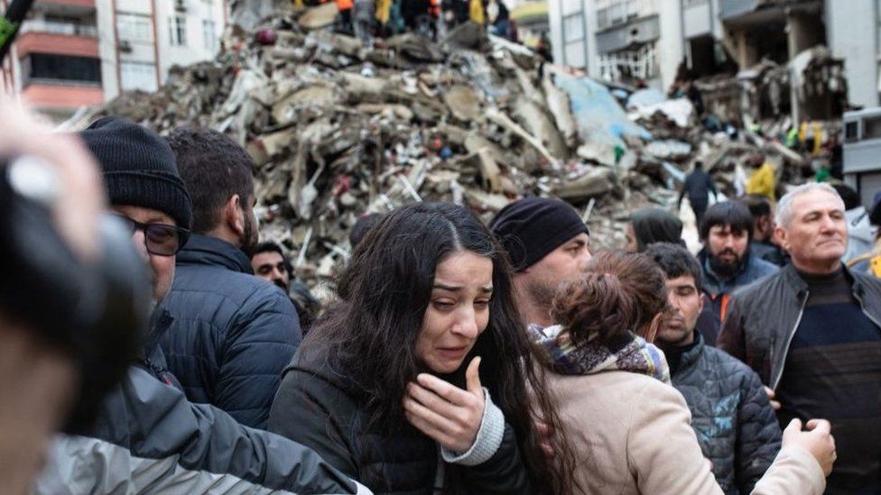 A woman in tears with a mound of rubble behind her.