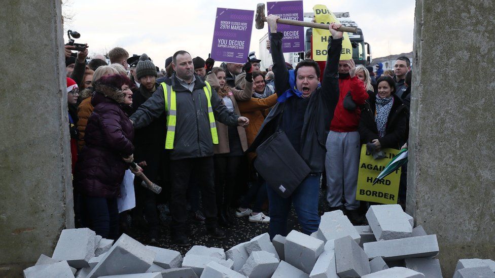 A man cheers after knocking dock a mock border wall at a Brexit protest near Newry