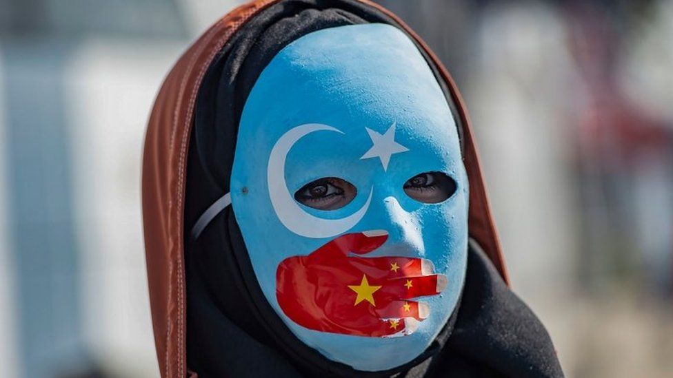 A protester against China's actions in Xinjiang wears a mask with the colours of the flag of East Turkestan