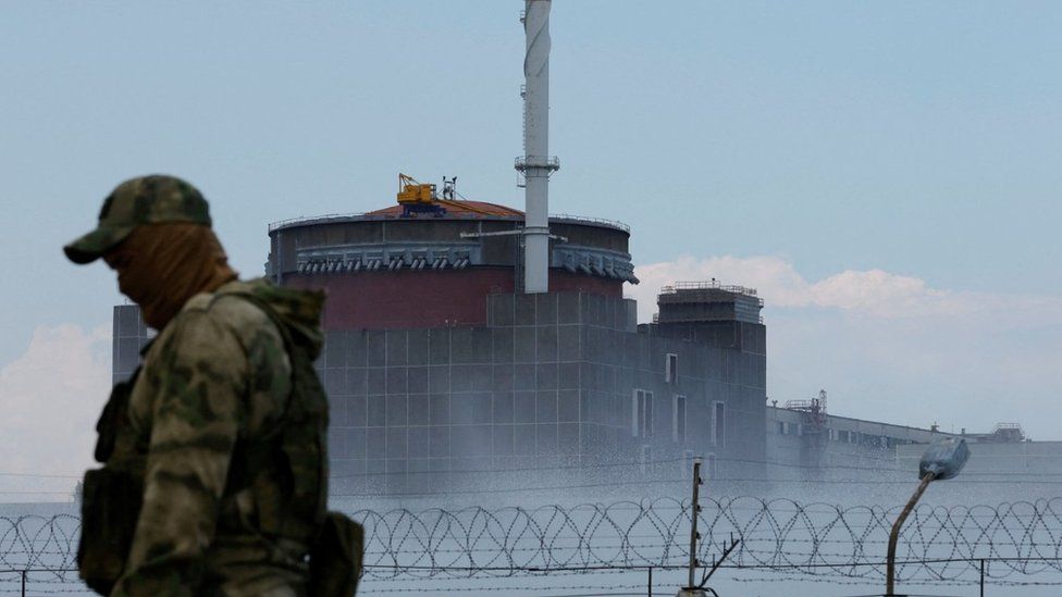 A serviceman with a Russian emblem  connected  his azygous   stands defender  adjacent   the Zaporizhzhia Nuclear Power Plant