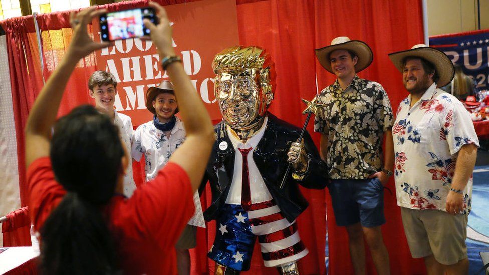 Посетители Cpac позируют с золотой статуей Дональда Трампа